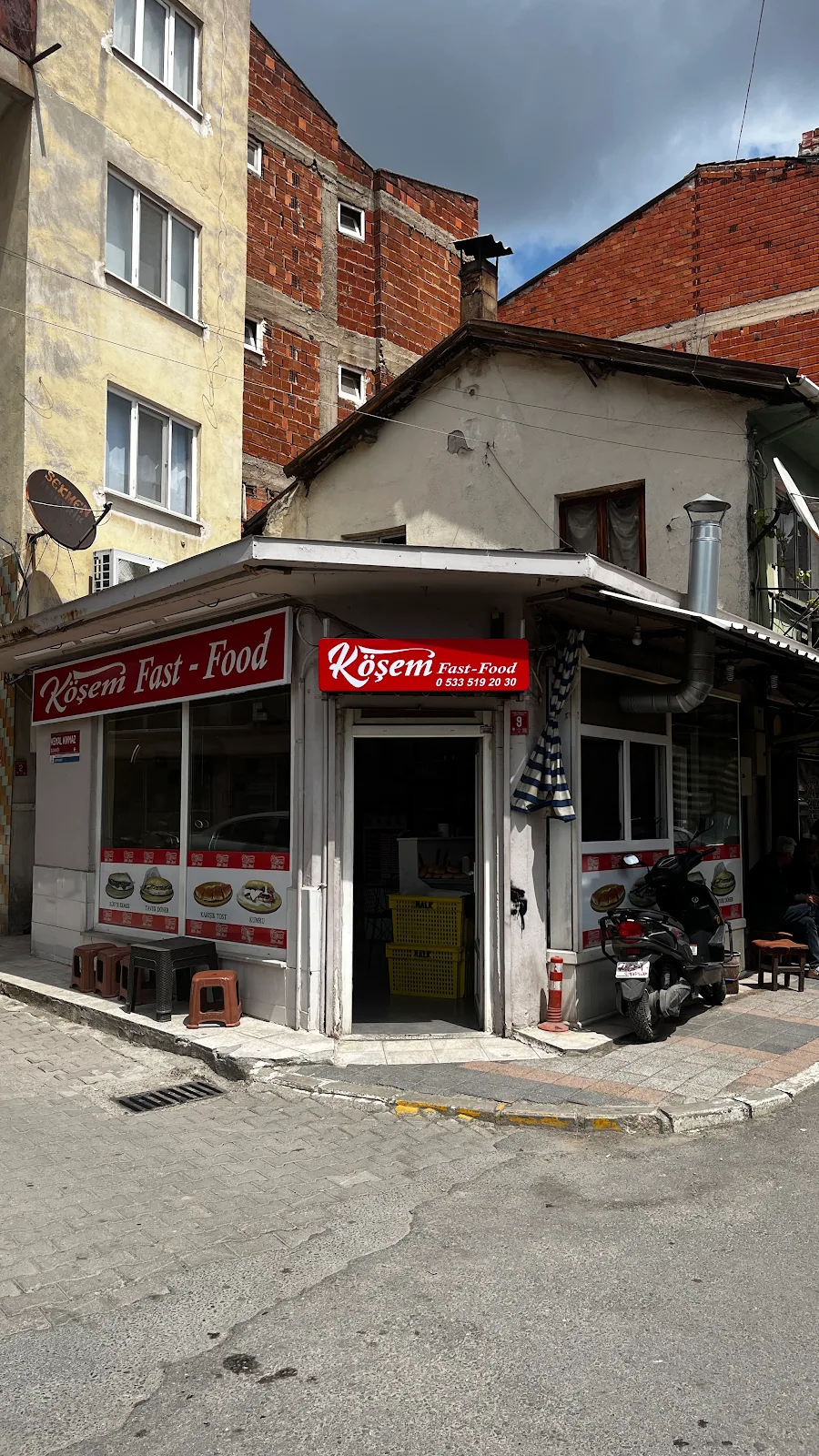 Köşem Fast Food dükkânının dışarıdan görünümü: köşe başında kırmızı Köşem tabelası, açık kapı ve önünde tabureler